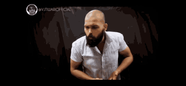 a bald man with a beard is standing in front of a black curtain with the hashtag @vjtilwariofficial on the bottom