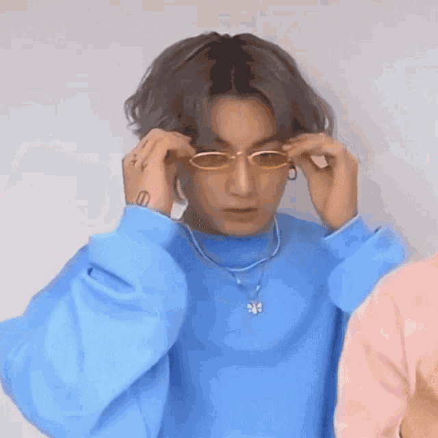 a young man wearing a blue sweater and sunglasses is adjusting his sunglasses .