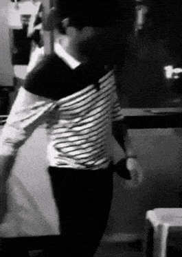 a man in a striped shirt is standing in front of a refrigerator in a black and white photo .