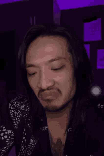 a man with long hair and a beard is making a face with his eyes closed