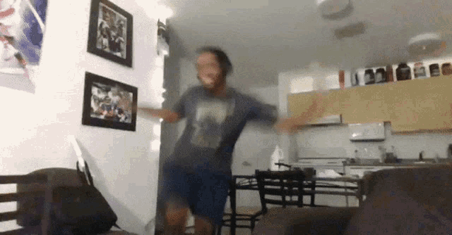 a man in a blue shirt is dancing in a living room with pictures on the wall