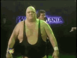 a man in a black tank top is standing in front of a sign that says w mania