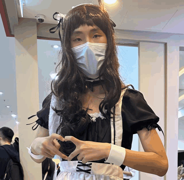 a woman in a maid costume is making a heart with her hands