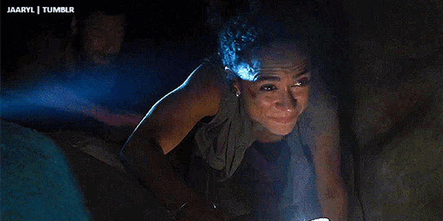 a woman with blue hair is standing in a dark room with a light shining on her face .