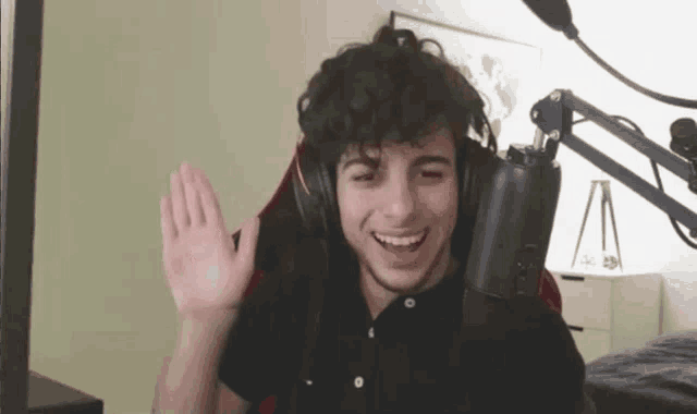 a young man wearing headphones is sitting in front of a microphone waving his hand .