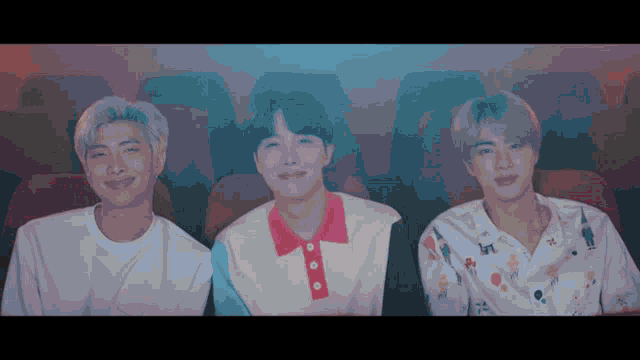 three young men are sitting next to each other in a dark room and smiling