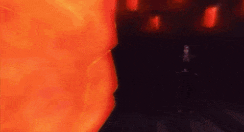 a man in a suit is standing in front of a large orange fireball in a dark room .