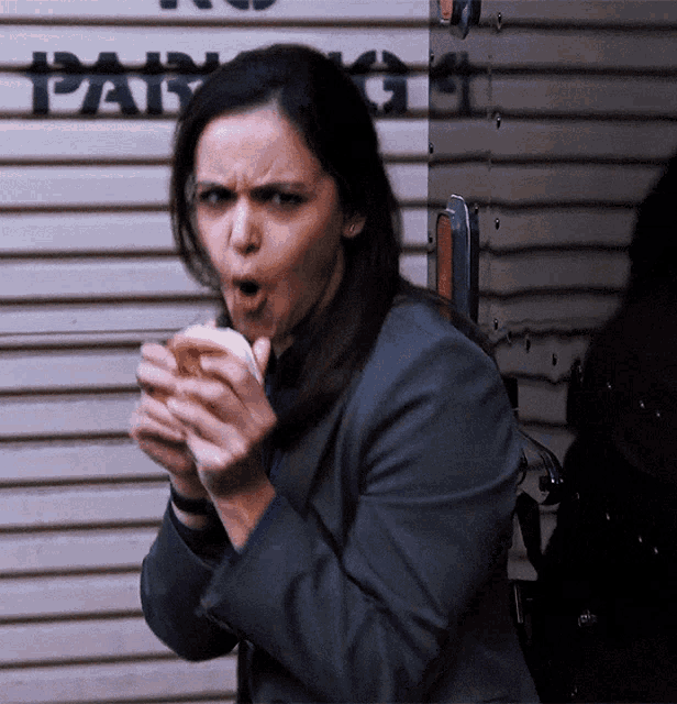 a woman in a suit is eating a sandwich in front of a wall with the word parking on it