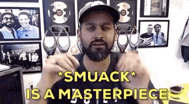 a man with a beard says smuack is a masterpiece in front of a wall of pictures