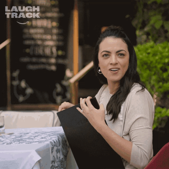 a woman sitting at a table with a menu in front of a sign that says " laugh track "