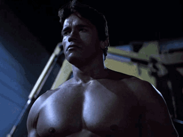 a shirtless arnold schwarzenegger stands in front of a yellow machine