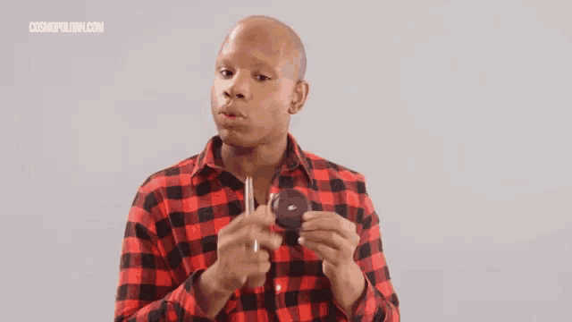 a man in a red and black plaid shirt is holding a small mirror in his hand .
