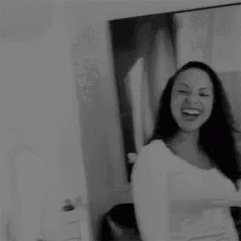 a woman in a white shirt is standing in front of a couch in a black and white photo .