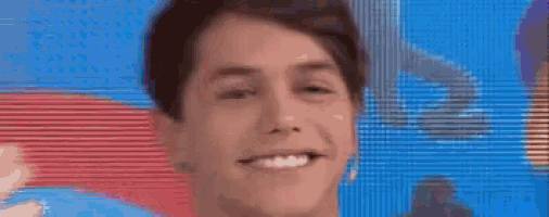 a young man is smiling in front of a large screen while holding his hair .