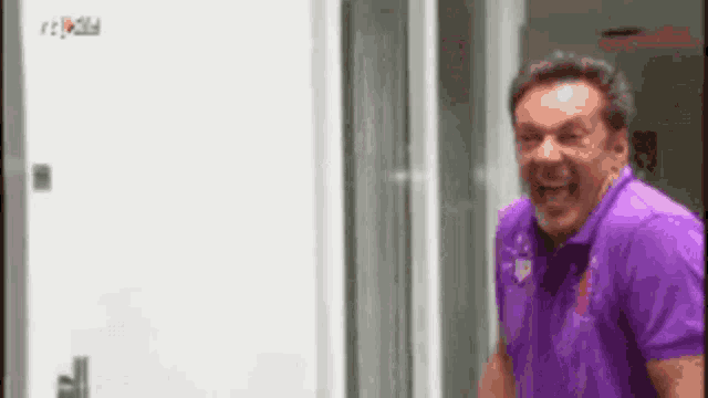 a man in a purple shirt is laughing while standing in front of a white door