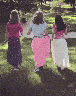 three girls in long skirts are walking in the grass