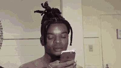 a shirtless man with dreadlocks is looking at his cell phone .