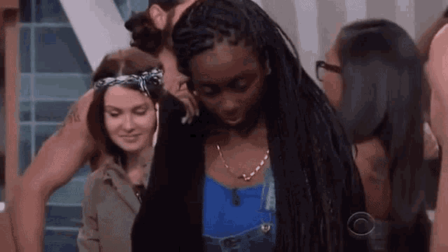 a group of people are standing around a woman with braids and a man hugging her .