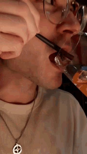 a man with glasses is drinking from a glass with chopsticks