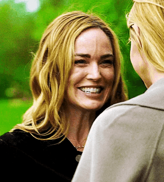 two women are smiling and looking at each other in front of a green background