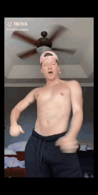 a shirtless man is dancing under a ceiling fan in a bedroom .