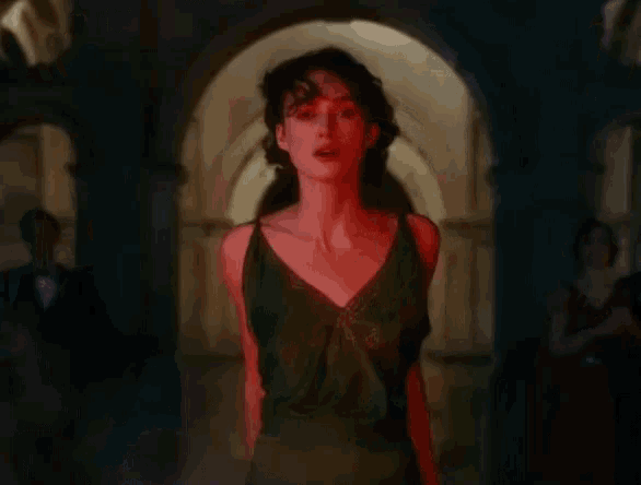 a woman in a green dress is standing in a hallway with a red light on her face .