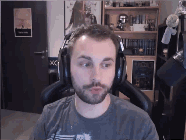 a man with a beard wearing headphones in front of a door that says x on it