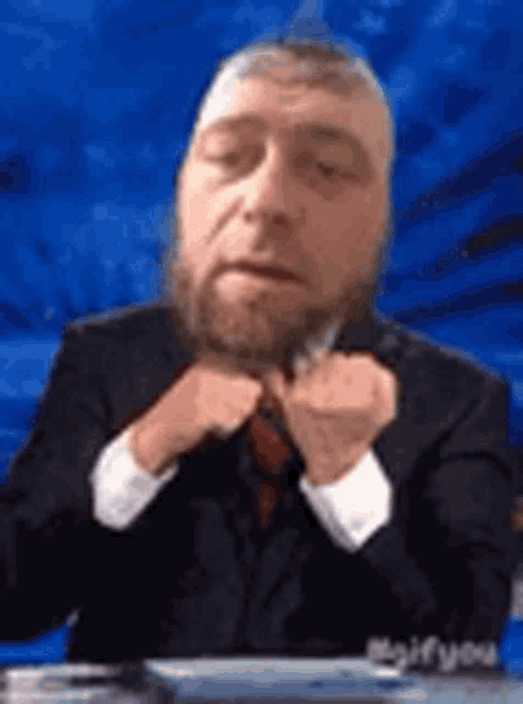 a man with a beard is wearing a suit and tie and sitting at a table .