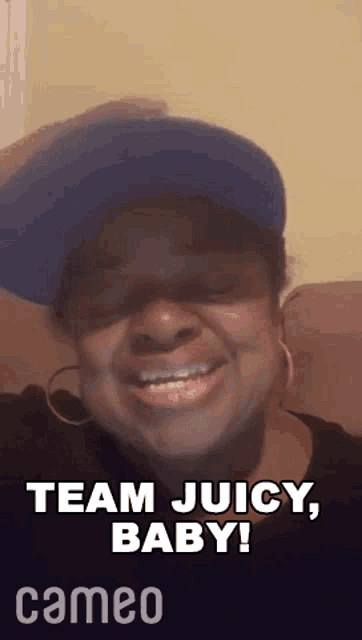 a woman wearing a blue hat and earrings is smiling and saying team juicy baby .