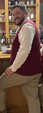 a man in a maroon vest is sitting on a bar stool