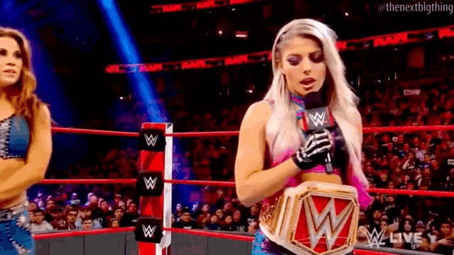 a woman is holding a microphone in a wrestling ring while standing next to another woman .