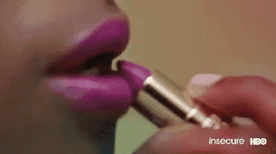 a close up of a woman applying purple lipstick on her lips .