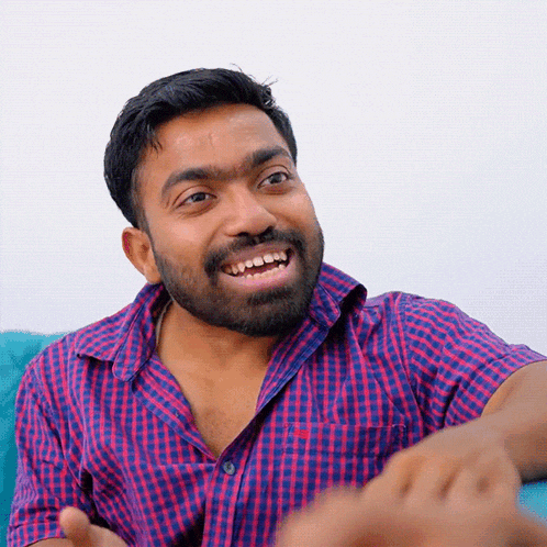 a man with a beard wearing a red and blue plaid shirt is smiling
