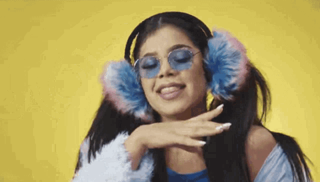 a woman wearing headphones , sunglasses , and ear warmers is dancing on a yellow background .