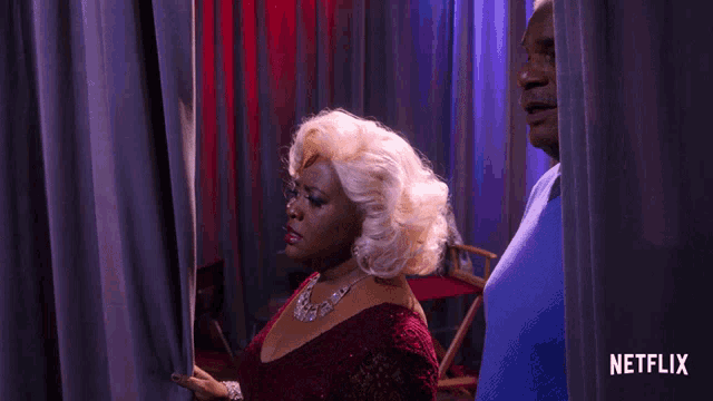 a woman in a red dress stands next to a man in a blue shirt behind a curtain that says netflix on it