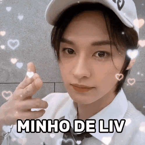 a young man wearing a hat and tie is making a heart shape with his fingers and the words minho de liv above him .