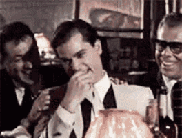 a group of men are sitting at a table laughing .