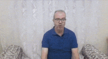 a man wearing glasses and a blue shirt is sitting on a couch .