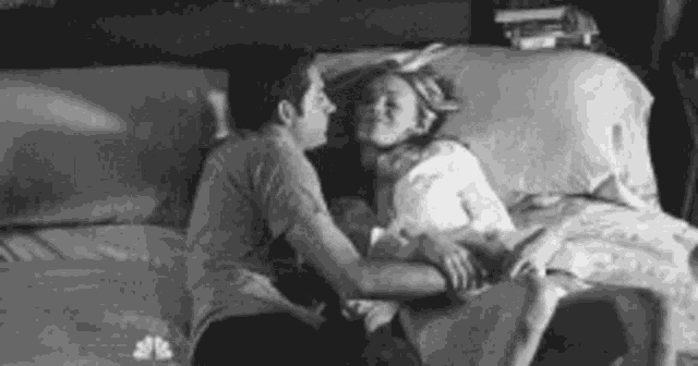 a black and white photo of a man and a woman kissing on a bed .
