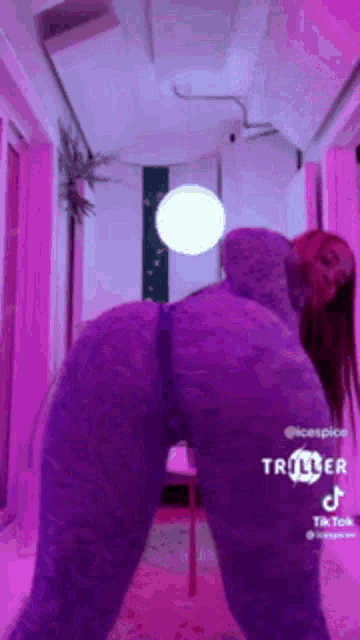 a woman in a purple outfit is standing in a room with purple lights .