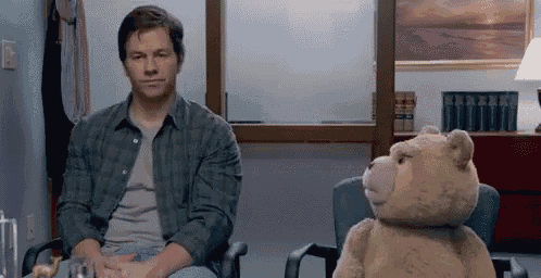 a man is sitting in a chair next to a stuffed bear .