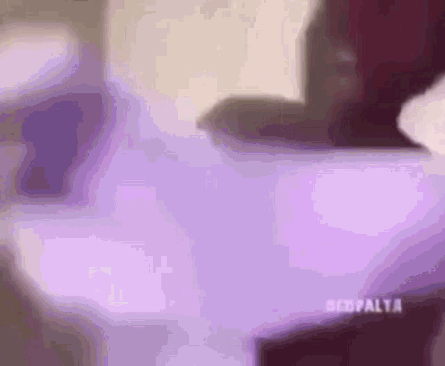 a blurry picture of a person laying on a bed with a purple blanket .
