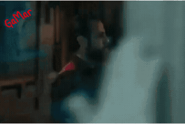a man with a beard is standing in a dark room with a sign that says gamar on it