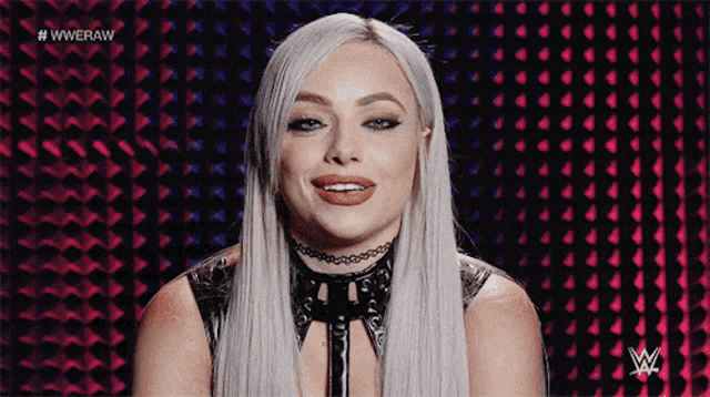 a woman with a choker on her neck is smiling in front of a wwe logo .