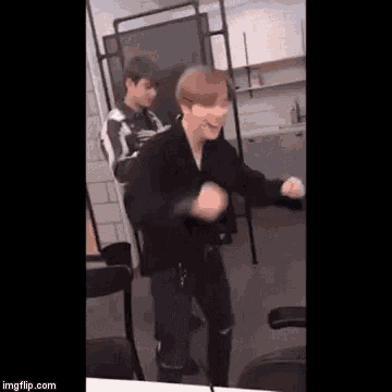 a man in a black jacket is dancing in a room while another man stands behind him .