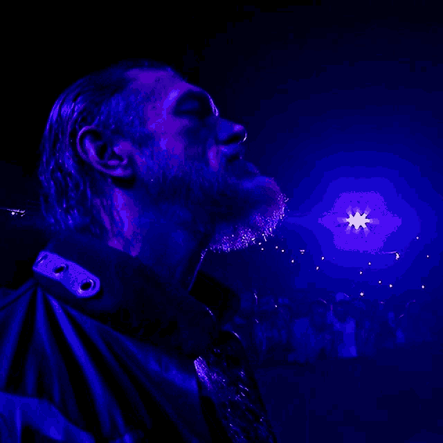 a man with a beard is standing in a dark room with a blue light behind him