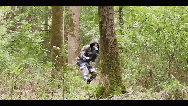 a person wearing a gas mask is standing next to a tree in a forest .
