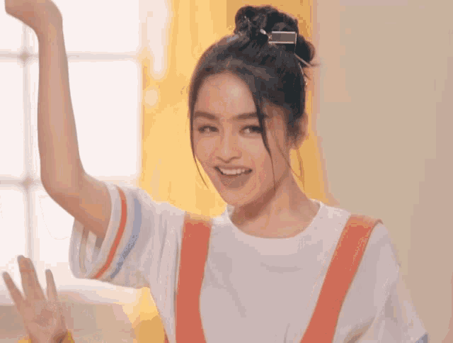 a woman in a white shirt and orange overalls is smiling with her arm in the air
