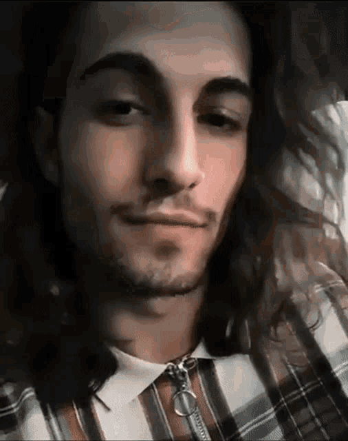 a man with long hair and a beard is wearing a plaid shirt with a zipper .