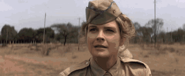 a woman in a military uniform stands in a field with trees in the background